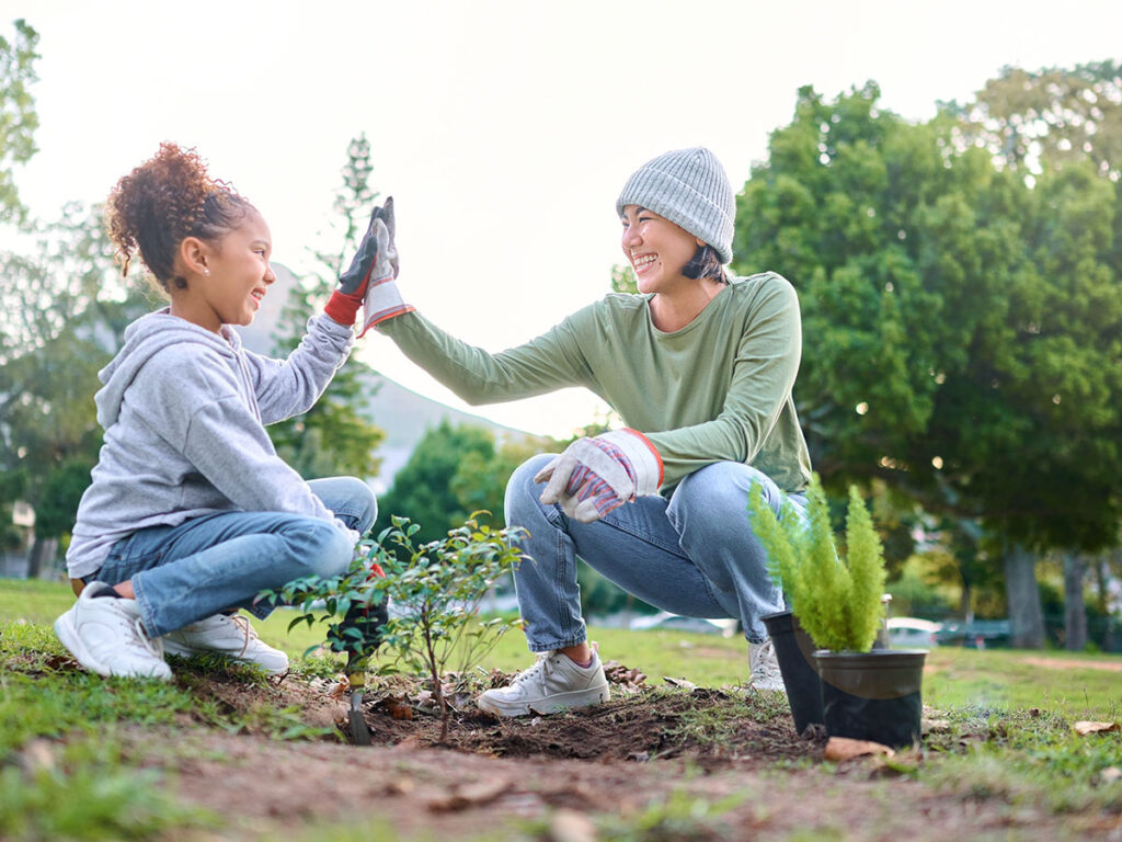 High five, child and woman with plant for gardening, ecology and agriculture in a park with trees. Volunteer family celebrate growth, nature and sustainability for community environment on Earth day.