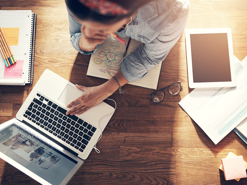 From above entrepreneur woman browsing laptop and holding pencil while thinking at laptop in office.