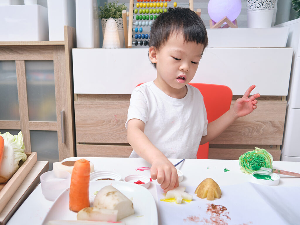 Asian kindergarten boy child making artwork from vegetable stamping at home