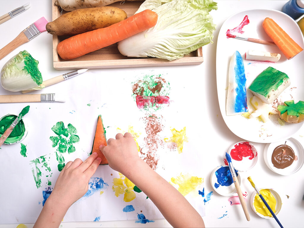 Top view close up of toddler boy child hands, kid making artwork from vegetable stamping at home, Fun art and crafts for toddlers, Children's Art Project